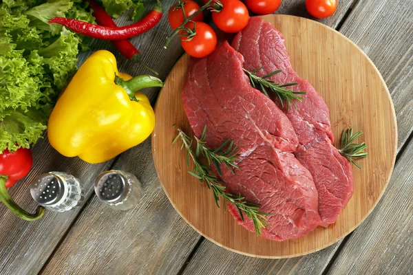 Bistecca di manzo cruda sul tagliere con verdure e spezie su fondo di legno — Foto Stock