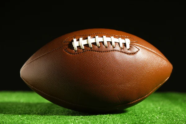 黒の背景に緑の草にアメリカン フットボール — ストック写真