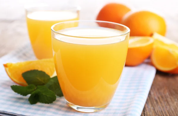 Glasses of orange juice with oranges on wooden table close up — Stock Photo, Image