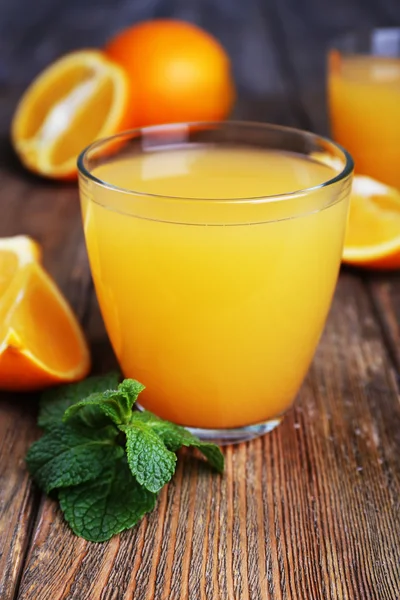 Gläser Orangensaft mit Orangen auf Holztisch in Großaufnahme — Stockfoto