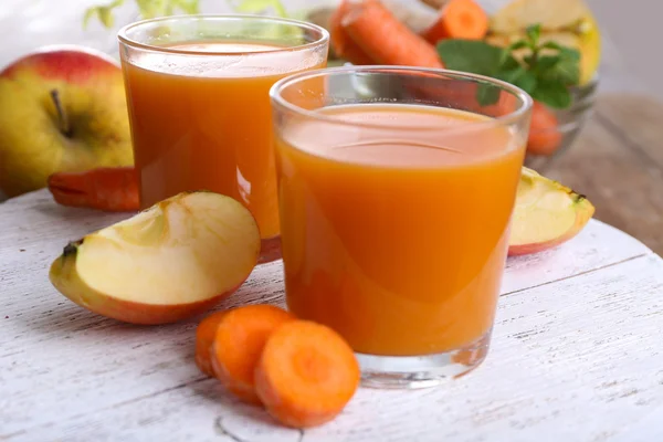 Glasses of juice with apple and carrot on wooden table close up