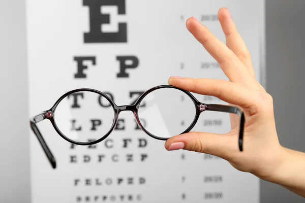 Glasses in hands on eye chart — Stock Photo, Image