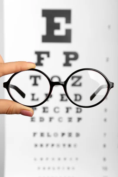 Glasses in hands on eye chart — Stock Photo, Image