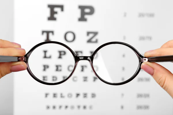 Glasses in hands on eye chart — Stock Photo, Image