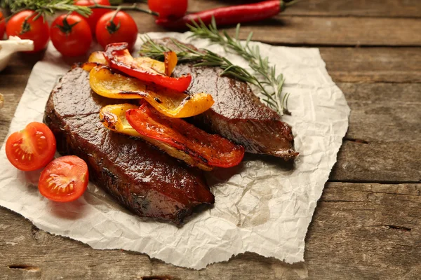 Kompozycja z smaczne mięso pieczone na papier arkusz, pomidory i rozmaryn gałązki na drewniane tła — Zdjęcie stockowe