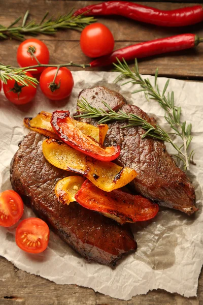 Composition with tasty roasted meat on paper sheet, tomatoes and rosemary sprigs on wooden background — Stock Photo, Image