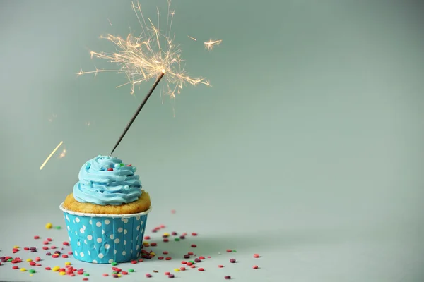 Cupcake with sparkler on grey background — Stock Photo, Image