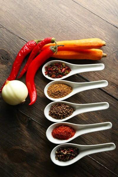 Different kinds of spices in ceramics spoons, close-up, on wooden background — Stock Photo, Image