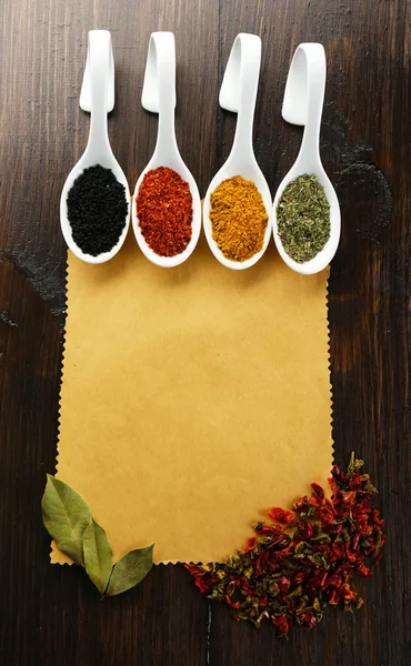 Olika sorters kryddor i keramik skedar på blankt papper blad på trä bakgrund — Stockfoto