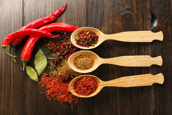 Different kinds of spices in spoons, close-up, on wooden background — Stock Photo, Image