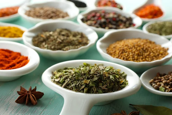 Different kinds of spices in ceramics spoons, close-up, on color wooden background — Stock Photo, Image