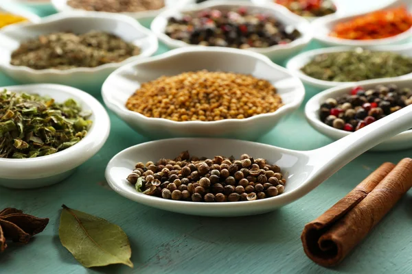 Different kinds of spices in ceramics spoons, close-up, on color wooden background — Stock Photo, Image