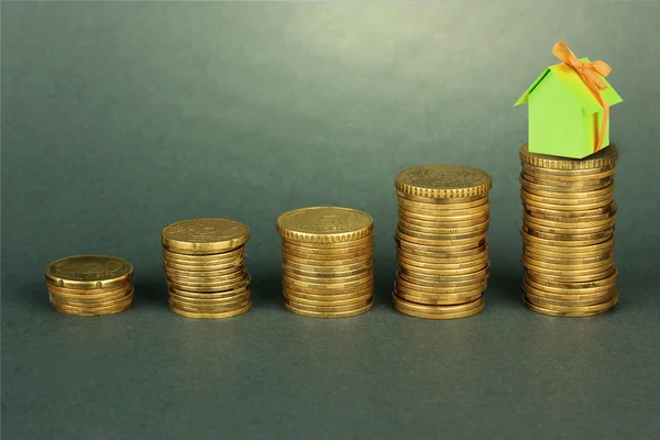 Small house standing on stack of coins on gray background — Stock Photo, Image