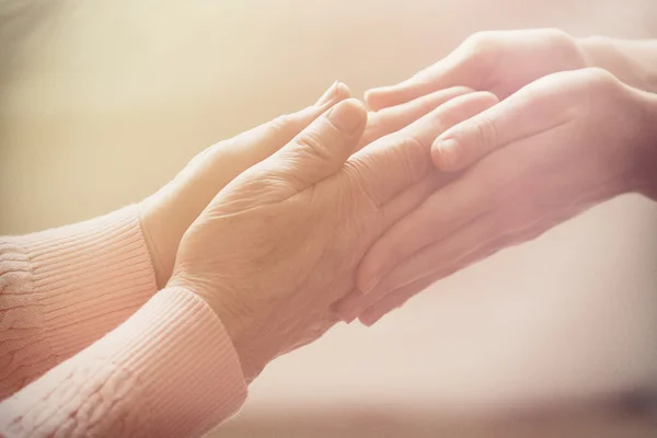 Old and young holding hands on light background, closeup — Stock Photo, Image