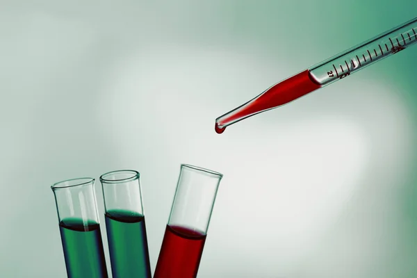 Pipette adding red fluid to the one of test-tubes on bright background — Stock Photo, Image