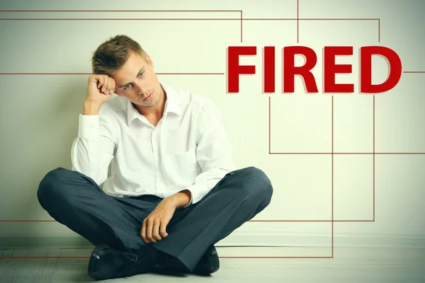 Sad fired office worker sitting on floor on wall background — Stock Photo, Image
