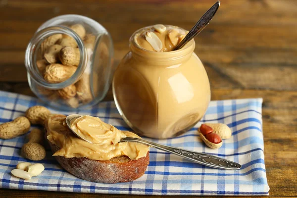 Saporito panino e barattolo con burro di arachidi fresco su sfondo di legno — Foto Stock