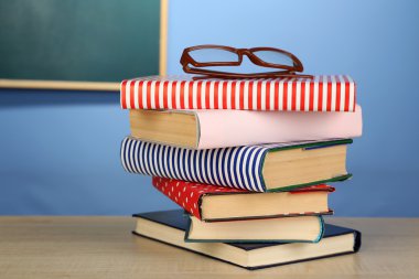 Ahşap masa, renkli duvar ve karatahta zemin üzerinde gözlüklü kitap yığını