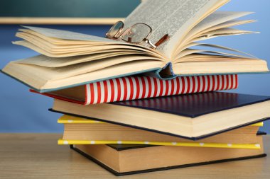 Ahşap masa, renkli duvar ve karatahta zemin üzerinde gözlüklü kitap yığını