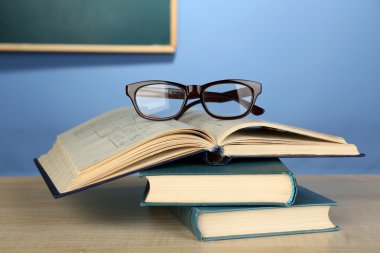 Ahşap masa, renkli duvar ve karatahta zemin üzerinde gözlüklü kitap yığını