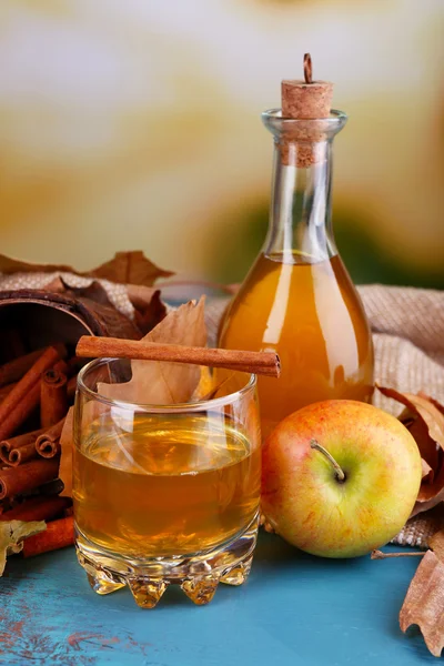 Komposition aus Apfelmost mit Zimtstangen, frischen Äpfeln und Herbstblättern auf Holztisch, auf hellem Hintergrund — Stockfoto