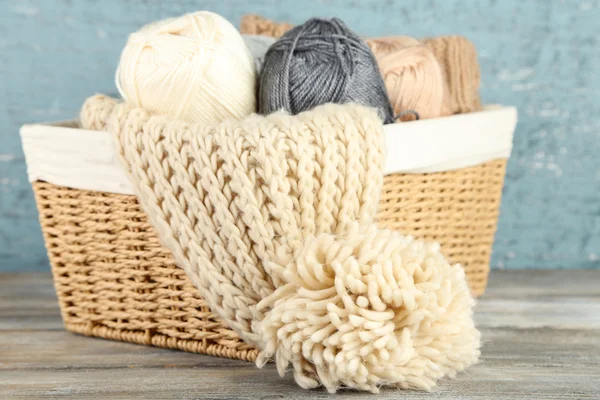 Knitting scarf and yarn in basket, on wooden background — Stock Photo, Image