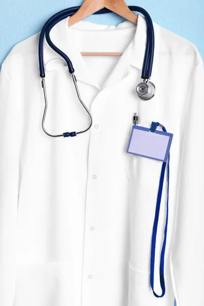 Arts jas met stethoscoop op hanger op blauwe achtergrond — Stockfoto