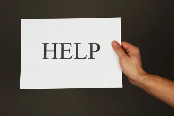 Лист бумаги с табличкой "Помощь" в мужской руке на темном фоне — стоковое фото