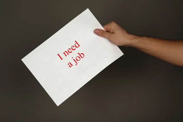 Sheet of paper with inscription I need a job in male hand on dark background — Stock Photo, Image