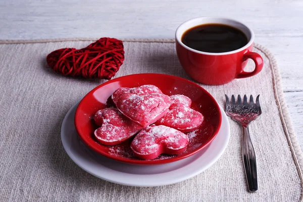 Cookies in vorm van hart op plaat met kop koffie op servet en kleur houten planken achtergrond — Stockfoto