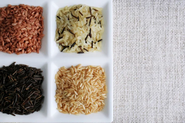 Diferentes tipos de arroz en plato sobre fondo de tela — Foto de Stock