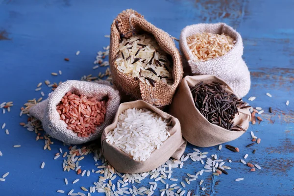 Different types of rice in sacks on wooden background — Stock Photo, Image