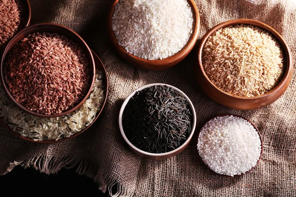 Různé druhy rýže v miskách na pozadí pytloviny — Stock fotografie