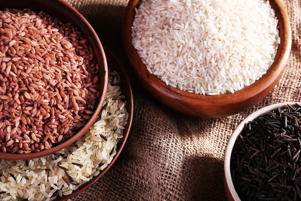 Diferentes tipos de arroz en cuencos sobre fondo de saco — Foto de Stock