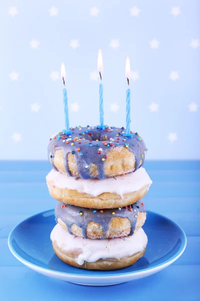 Delicious donuts with icing and birthday candles on table on bright background — Stock Photo, Image