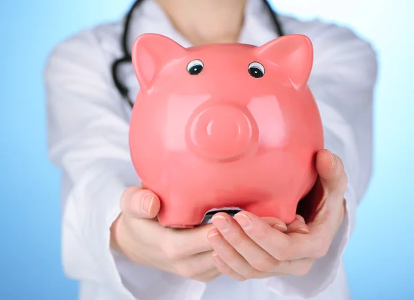 Doctor con alcancía rosa sobre fondo azul, de cerca — Foto de Stock