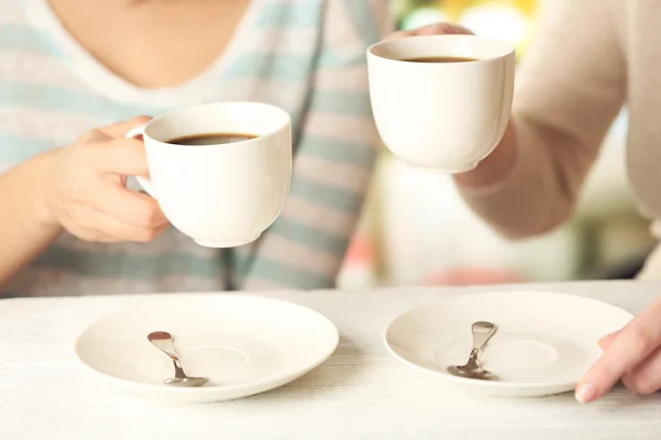 Dos mujeres con tazas de café sobre fondo brillante — Foto de Stock