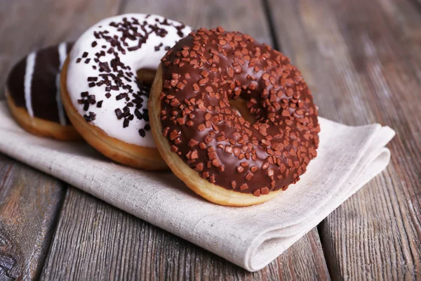 Deliciosos donuts com cobertura em guardanapo em fundo de madeira — Fotografia de Stock