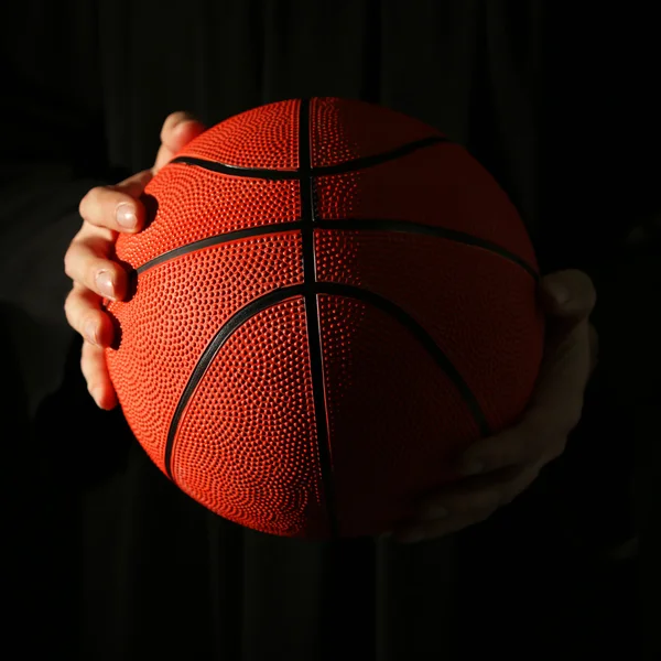 Mains masculines tenant ballon de basket sur fond sombre — Photo