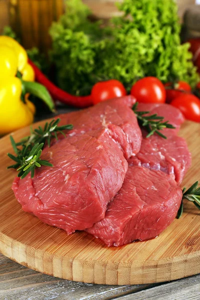 Raw beef steak on cutting board with vegetables and greens on wooden background — Stock Photo, Image