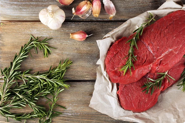 Biberiye ve sarımsak ahşap arka plan üzerinde kağıt üzerinde ham sığır eti biftek — Stok fotoğraf