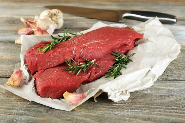 ローズマリーとニンニクの木製の背景紙の上で牛肉ステーキ — ストック写真