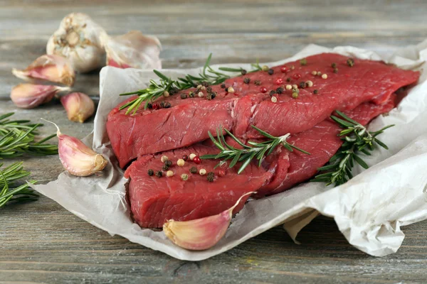 Syrové hovězí steak s rozmarýnem a česnekem na papíře o dřevěné pozadí — Stock fotografie