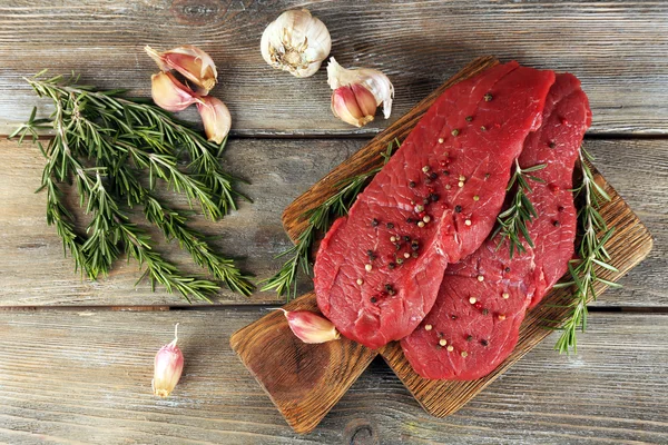 Rauwe biefstuk met rozemarijn en knoflook op snijplank op houten achtergrond — Stockfoto