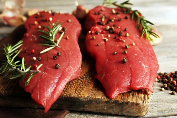 Syrové hovězí steak s rozmarýnem a koření na prkénko na dřevěné pozadí — Stock fotografie