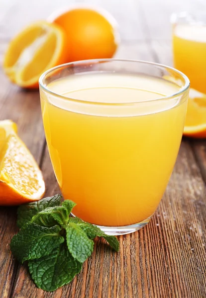 Glas apelsinjuice med apelsiner på träbord nära håll — Stockfoto