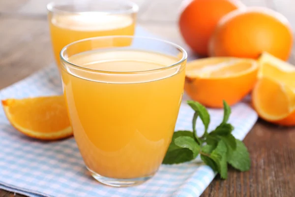 Óculos de suco de laranja com laranjas na mesa de madeira de perto — Fotografia de Stock