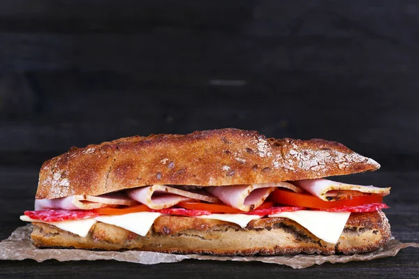 Fresh and tasty sandwich with ham and cheese on paper on wooden background — Stock Photo, Image