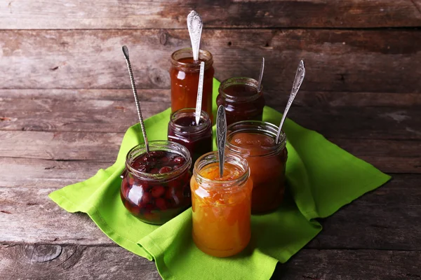 Jars of tasty jam with napkin on wooden background — Stock Photo, Image