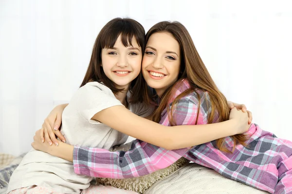 Zwei Mädchen im Pyjama sitzen auf einem flauschigen weißen Teppich vor hellem Hintergrund — Stockfoto